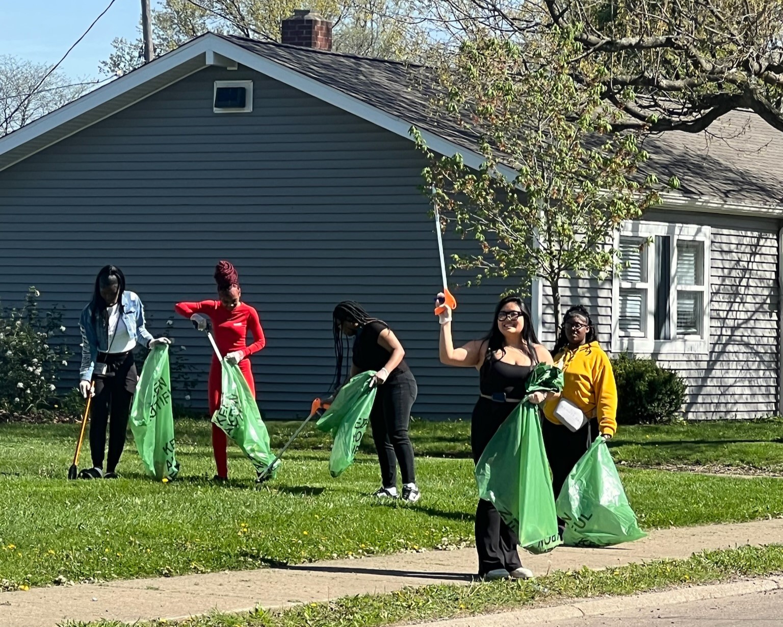 A group of community members collecting litter in green bags along a neighborhood street